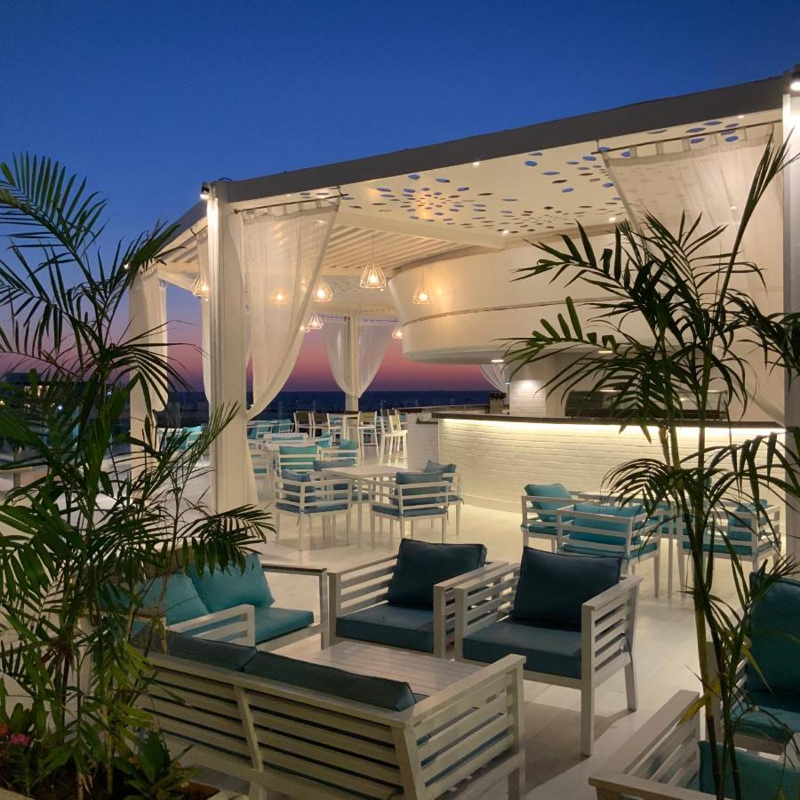 Sunrise Alex Avenue Hotel Alexandria Exterior photo The photo shows a stylish outdoor terrace or rooftop lounge area. It features white furniture, including comfortable seating with teal cushions. The space is adorned with draped sheer curtains, providing a relaxed and elegant atmosphere. Lush green p