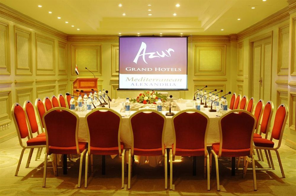 Sunrise Alex Avenue Hotel Alexandria Exterior photo The photo shows a conference room set up for a meeting or event. There is a large oval table surrounded by red chairs, and the table is equipped with microphones and bottles of water. In the background, there is a projector screen displaying the logo