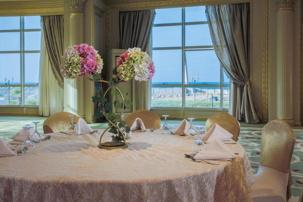 Sunrise Alex Avenue Hotel Alexandria Exterior photo The photo depicts a beautifully arranged round dining table set in an elegant room. The table is covered with a light-colored lace tablecloth and features an artistic floral centerpiece with pink and white flowers. The place settings include folded n