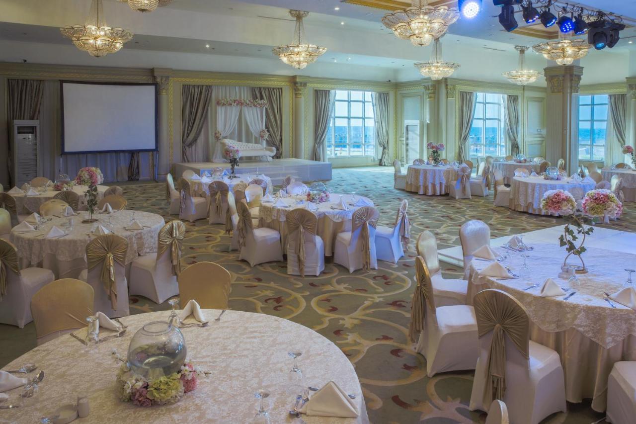 Sunrise Alex Avenue Hotel Alexandria Exterior photo The photo shows an elegantly designed banquet hall set up for an event. There are several round tables covered with light-colored tablecloths, each adorned with decorative centerpieces, such as floral arrangements. The chairs are draped with fabric t