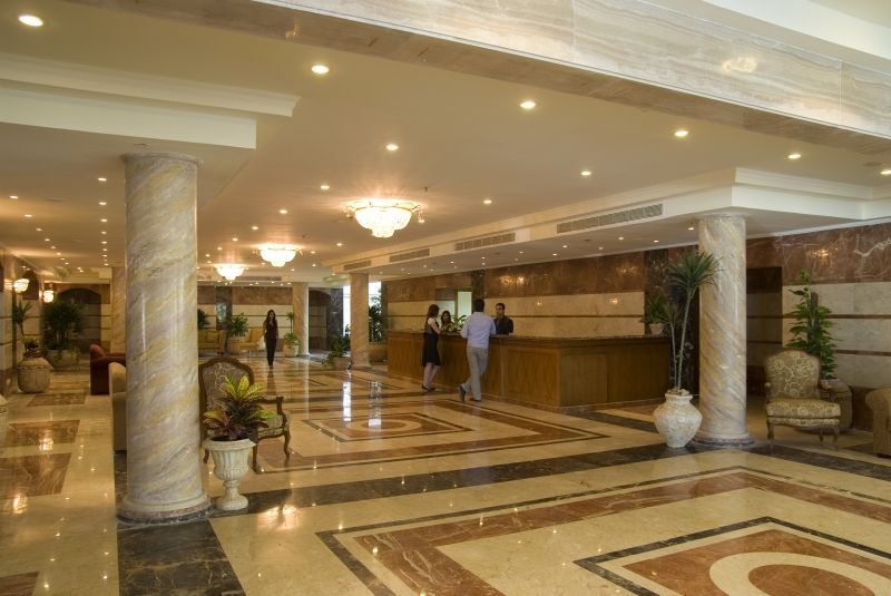 Sunrise Alex Avenue Hotel Alexandria Exterior photo The photo shows the interior of a spacious lobby, likely in a hotel. There are marble floors with intricate patterns, elegant lighting fixtures, and tall pillars. In the center, there is a reception desk where staff members are attending to guests. S